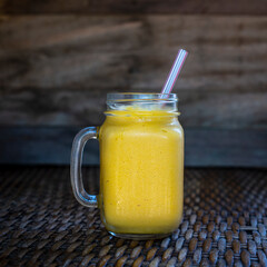 Fresh organic mango smoothie in glass mug on wooden table