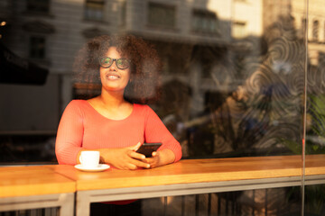 Young woman at cafe drinking coffee and using mobile phone. Beautiful African woman typing a message.