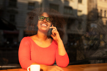 Young woman at cafe drinking coffee and using mobile phone. Beautiful African woman talking to the phone.