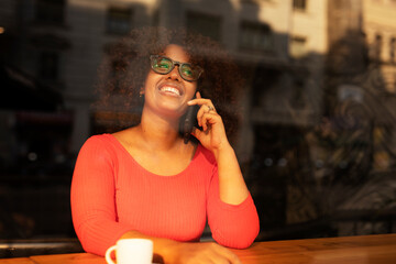 Young woman at cafe drinking coffee and using mobile phone. Beautiful African woman talking to the phone.