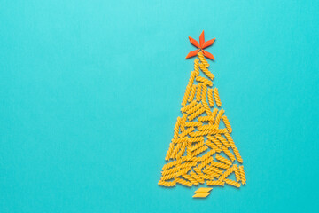 Abstract Christmas tree of raw pasta on a turquoise paper background. Top view, flat lay. Creative layout