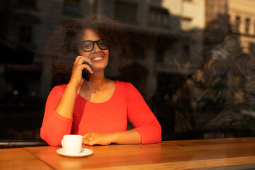 Young woman at cafe drinking coffee and using mobile phone. Beautiful African woman talking to the phone