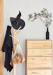 Halloween concept. Black hat, witch cloak and mesh bag with pumpkins on the hanger. Minimalist...