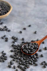 Fototapeta na wymiar Wooden spoon full of dry black beans on grey table