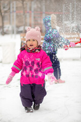 A little girl in a warm rose jumpsuit and a cap with bear ears smiles.