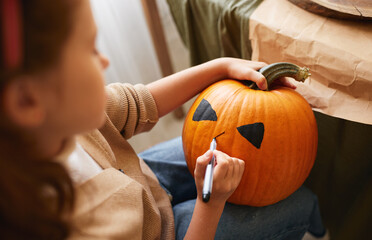 Little kid girl making Jack-o-lantern while preparing for Halloween party at home