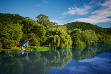 beautiful landscape of blue lake surrounded by lush trees with moored wooden boat and blue house