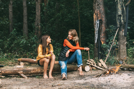 A mother with her teenage daughter is sitting on a tree near a campfire in the forest or park during a picnic. Weekends, vacations, time together