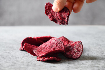 Take a piece vegetable beetroot chips on a gray background. Vegan snack. Close up.