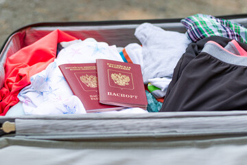 An open suitcase with things and two passports lies on the road on a sunny summer day. Selective focus