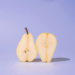 Two halves of pear fruit standing upright in hard light on purple blue background. Minimal food design