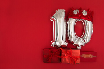 Foil silver air balloons showing number 10 ten placed on red background with wrapped presents for...