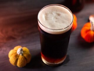 Seasonal autumn pumpkin beer, a glass of craft beer on a dark wooden table, knitted pumpkins