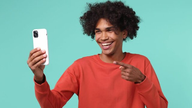 Overjoyed happy young curly african american man 20s wears azure t-shirt doing selfie shot on mobile phone post photo on social network isolated on plain pastel light blue background studio portrait