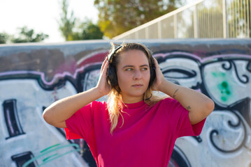 Portrait of sporty young woman in headphones. Girl in crimson dress standing near wall with graffiti, listening to music. Looking sideways. Sport, hobby, active lifestyle concept
