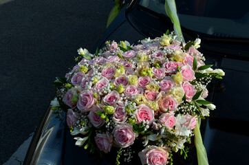wedding decoration of a black sports limousine where the flower is attached with a suction cup to the hood. pink roses dominate the flat round bouquet. green ribbon