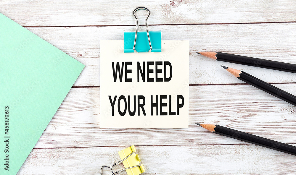 Poster stickers with pencils and notebook with text we need your help on wooden background