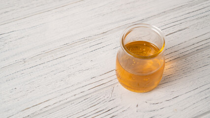 The portion of honey in the simple jar on a white wooden table. Detail of open honey jar. Honey bubbles in a glass jar