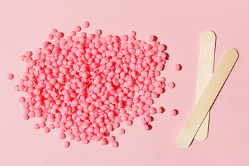 Beautiful pink depilatory wax granules and wooden spatulas on a pink background. Epilation, depilation, unwanted hair removal. Top view. - obrazy, fototapety, plakaty