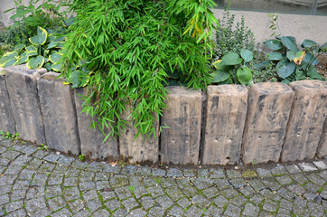 above the palisade of wooden sleepers are planted ornamental perennials and a very nice dwarf bamboo. arch by the road made of cobblestones