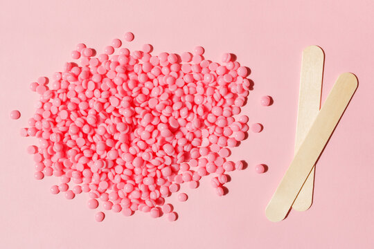 Beautiful pink depilatory wax granules and wooden spatulas on a pink background. Epilation, depilation, unwanted hair removal. Top view.