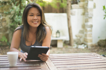 Attractive Japanese young woman using tablet in outdoor cafe. Beautiful girl shopping or chatting online, having fun, reading, freelancer working. Drinking coffee. Modern technology concept