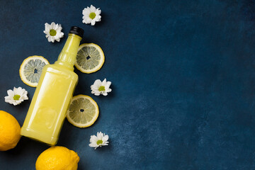 Limoncello bottle with lemons and flowers on blue background top view