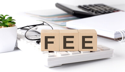 FEE written on a wooden cube on keyboard with office tools