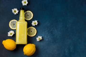 Limoncello bottle with lemons and flowers on blue background top view