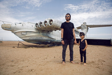 family a boy and his father in rocker clothes stand at an abandoned ekranoplan plane