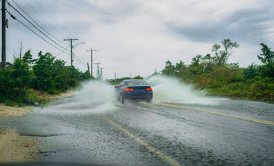 Flooded coastal road with a car splashing through in the rain 