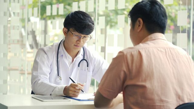 Asian doctor is examining the abnormal items of the body and diagnosing the disease in the paper with the medical report of the patient.