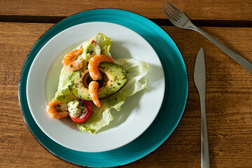 Fresh organic salad with avocado, tomato, shrimp, olive oil and herbs on a wooden table, top view