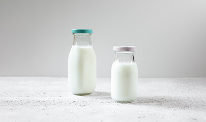 Two glass reusable bottles of fresh organic milk or dairy product on a white wooden table