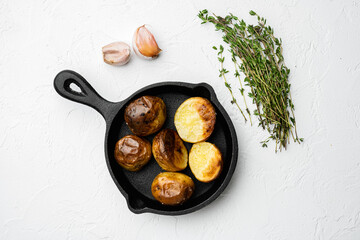 Baked potatoes , in frying cast iron pan, on white stone table background, top view flat lay