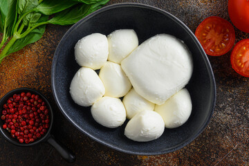 Tasty mozzarella cheese with basil and tomatoes in black bowl, ingredients for salad Caprese. on...
