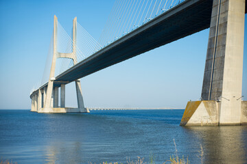 Big modern bridge over water. White suspension bridge over calm blue river. City architecture concept