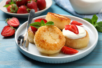 Delicious cottage cheese pancakes with strawberries, honey and sour cream on light blue wooden table, closeup
