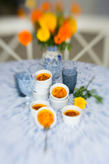 French dessert creme brulee with caramel crust in white baking molds on blue and white tablecloth and a bouquet of yellow and red marigolds flowers