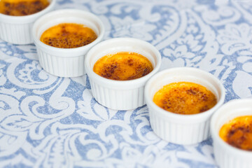 French dessert creme brulee with caramel crust in white baking molds on blue and white tablecloth 