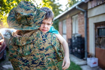 Crying little boy and soldier in a military uniform say goodbye before a separation. Soldier dad...
