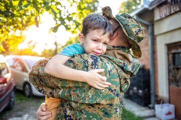 An emotional military father, dressed in camouflage, holds his young son in arms in greeting after returning home from a tour of duty overseas. Family and emotions Concept.