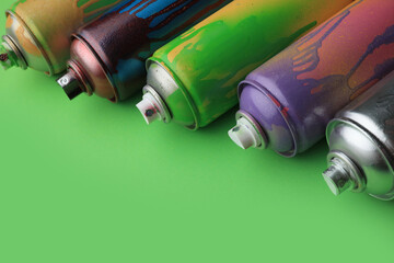 Used cans of spray paints on green background, closeup with space for text. Graffiti supplies