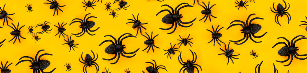 Flat lay pattern banner of black horror spiders of different sizes directed in different directions on orange backdrop with copy space. Halloween decoration spooky background concept for holidays