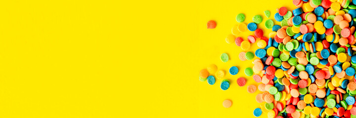 Fototapeta na wymiar Colorful round candies are neatly scattered on a yellow background. The banner. Flat lay, top view