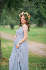Portrait of a young pregnant woman with a wreath on her head in the park.
