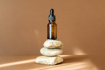 Mock-up of glass dropper bottle stands on improvised stand made of three stones. Rays of sunlight,...
