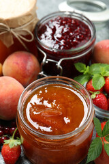 Jars with different jams and fresh fruits on table, closeup