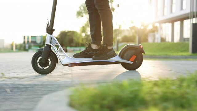 Legs man in black sneakers ride on electric mobile scooter. Modern Man Using Electric Scooter in Sunny Day. Adult man riding electric scooter to work. Eco friendly transportation