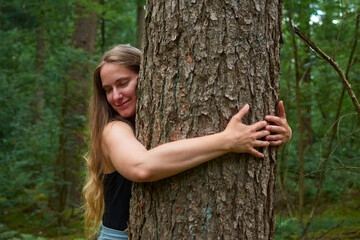 A blonde Caucasian lady with long hair hugging a tree in the forest